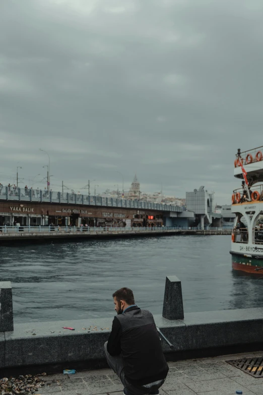 a man taking a picture of a boat in the water, istanbul, gray skies, sitting under bridge, 2019 trending photo