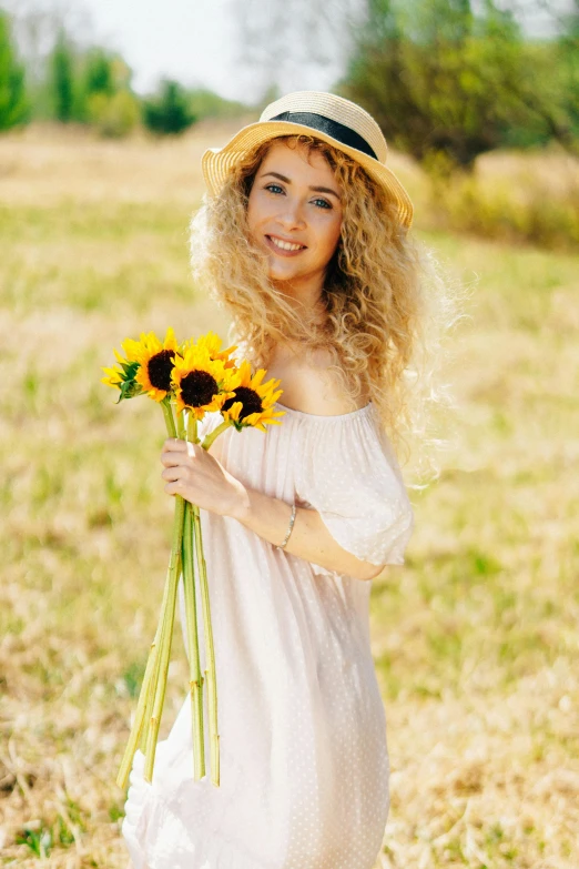 a woman holding a bunch of sunflowers in a field, pexels, renaissance, long fluffy blond curly hair, square, happy fashion model, with hat