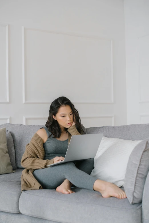 a woman sitting on a couch using a laptop, trending on pexels, dressed in a gray, asian human, hunting, brunette woman