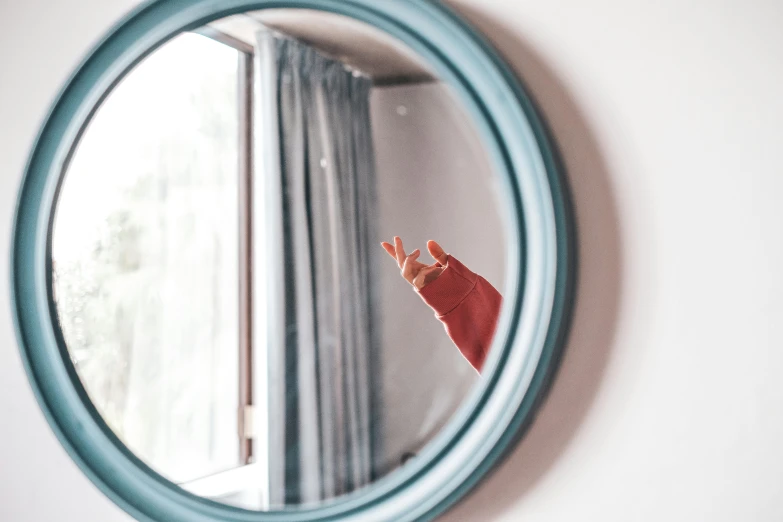 a person standing in front of a mirror making a peace sign, inspired by Elsa Bleda, pexels contest winner, visual art, light red and deep blue mood, round window, zoomed in, family friendly