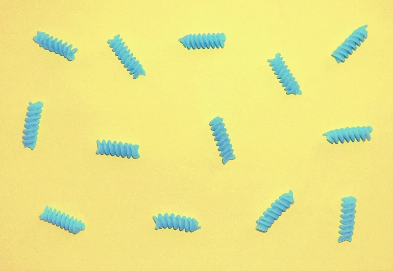 a bunch of blue screws sitting on top of a yellow surface, a microscopic photo, by Rachel Reckitt, trending on pexels, op art, candy worms, fish tail, made of candy, intricate pasta waves