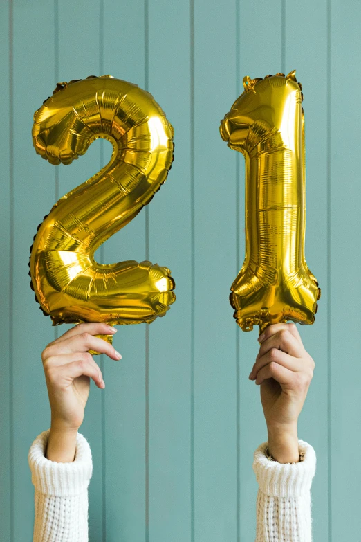 a person holding up two gold balloons in the air, by Julia Pishtar, shutterstock, happening, thin aged 2 5, celebrating a birthday, 2 1 st century, 2 colours