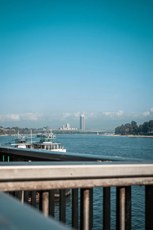 a large body of water next to a bridge, a picture, inspired by Paul Gustav Fischer, unsplash, vallejo, boat in foreground, blue sky, full frame image