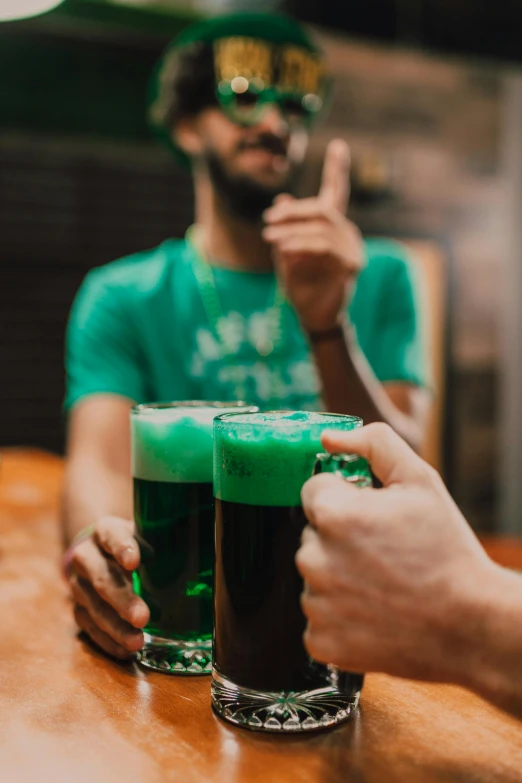 a couple of people that are sitting at a table, holding a mug of beer, emeralds, 2019 trending photo, man?