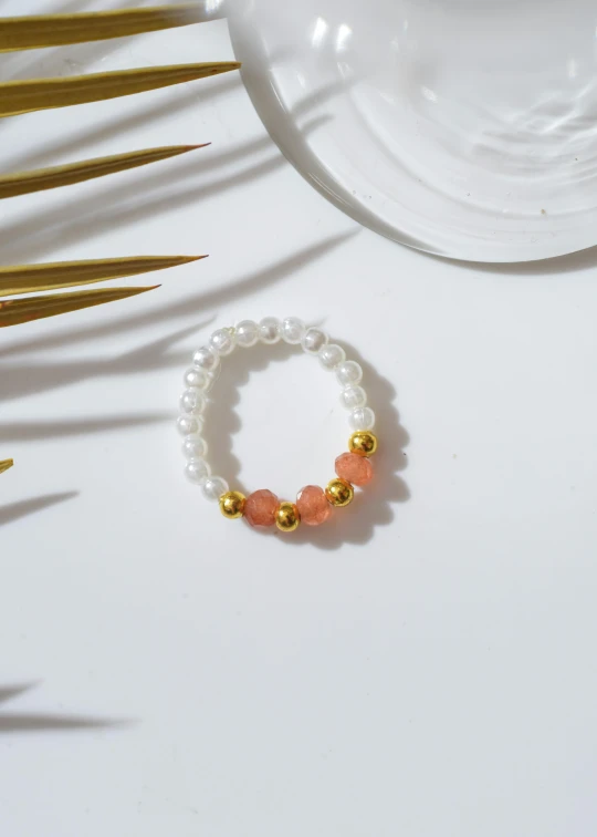 a close up of a bracelet on a table, by Emma Andijewska, baroque, orange and white, jakarta, chillhop, pearls