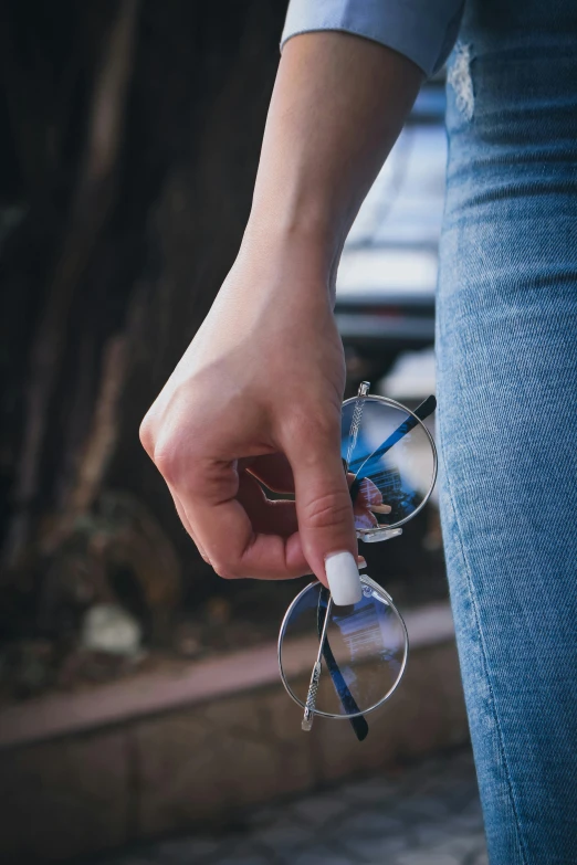 a close up of a person holding a pair of glasses, wearing jeans, lens flair, scissors in hand, round sunglasses