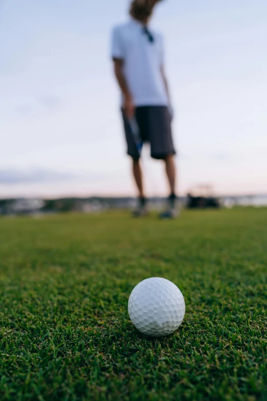 a man standing on top of a lush green field next to a golf ball, in the evening, oceanside, up close, off - putting