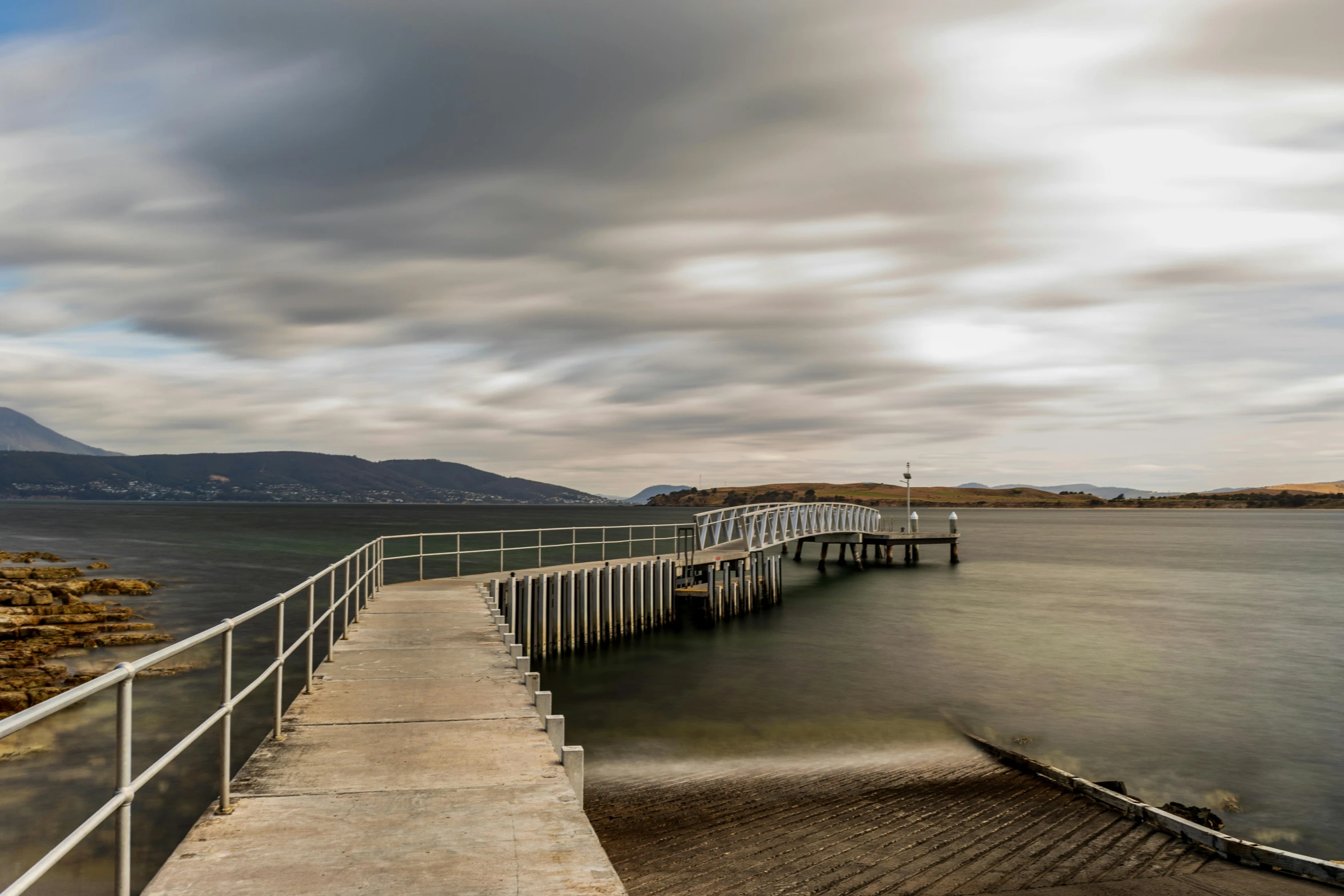 a pier next to a body of water under a cloudy sky, a portrait, kilart, landscape photo, brown, voge photo