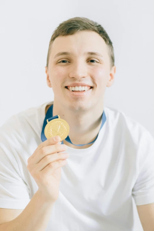 a man in a white shirt holding a gold medal, inspired by Ryan Pancoast, pexels contest winner, on a white table, headshot profile picture, max bedulenko, he is about 20 years old | short