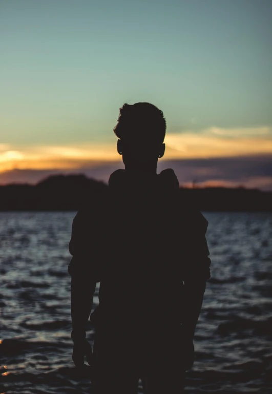 a silhouette of a person standing in the water, looking off into the distance, over his shoulder, profile picture 1024px, human staring blankly ahead