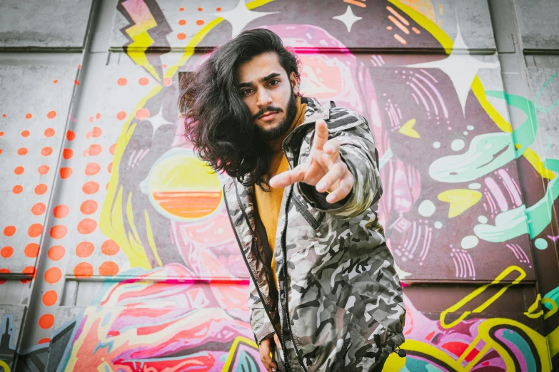 a man standing in front of a graffiti covered wall, an album cover, by Adam Dario Keel, trending on pexels, graffiti, mid long hair, shabab alizadeh, pointing, headshot profile picture