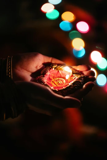 a person holding a lit diya in their hands, pexels, festive colors, instagram post, ornament, light bloom