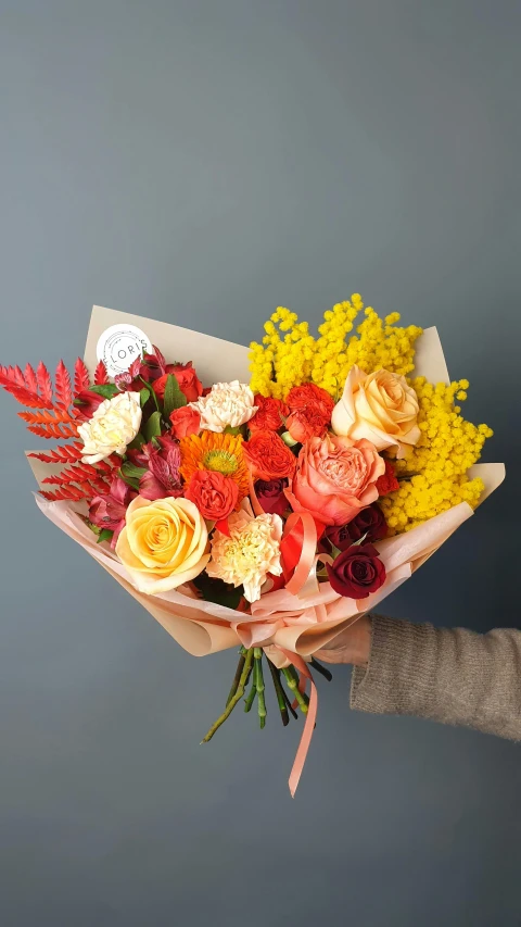 a person holding a bunch of flowers in their hand, dark oranges reds and yellows, full product shot, roses and lush fern flowers, paper chrysanthemums