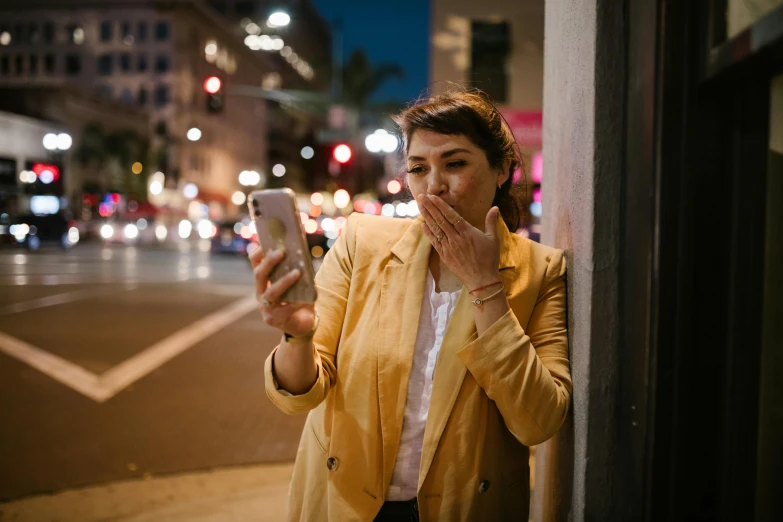 a woman standing on the side of a street looking at her cell phone, pexels contest winner, happening, fleshy creature above her mouth, evening time, yellow hue, androgynous person