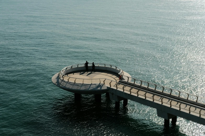 a couple of people standing on top of a pier, by Niko Henrichon, pexels contest winner, hurufiyya, curvilinear architecture, near the sea, overpass, circular