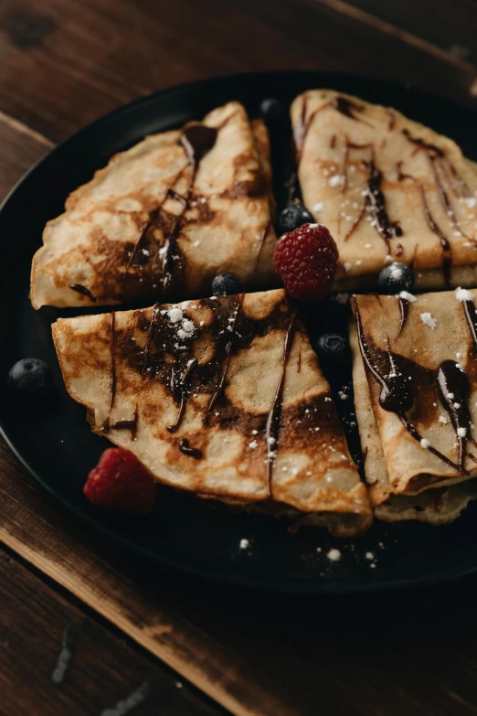 a black plate topped with pancakes covered in syrup, a portrait, unsplash, chocolate, folded, fruit, rustic