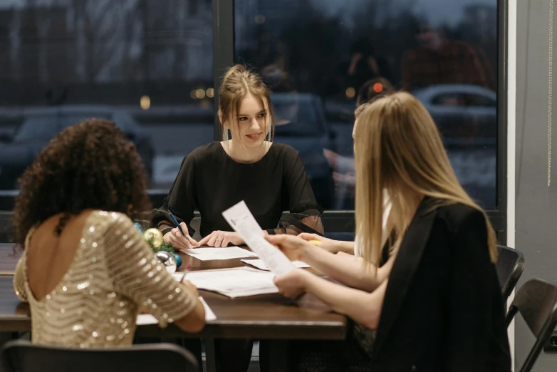 a group of women sitting around a wooden table, on a desk, fast paced, thumbnail, slight overcast lighting