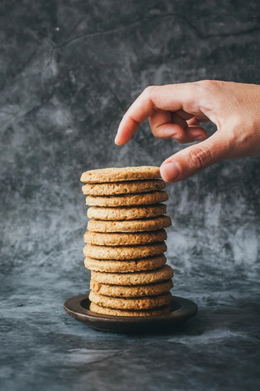 a person reaching for a stack of cookies, inspired by Richmond Barthé, on textured disc base, standing with a black background, circular towers, silo