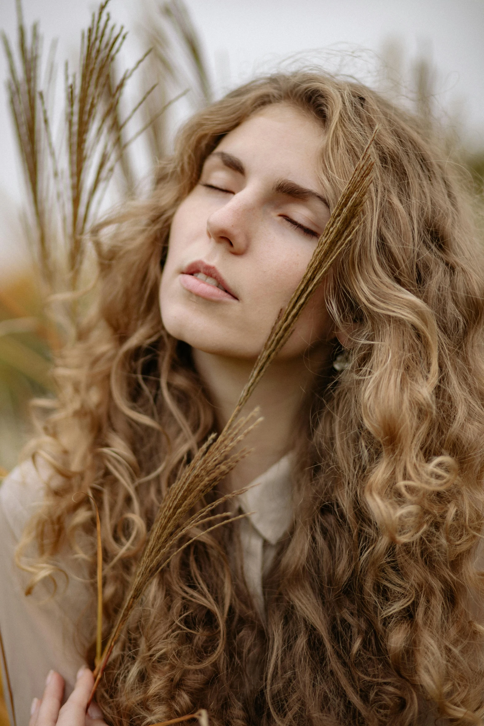 a woman with long curly hair standing in a field, trending on pexels, sleepy fashion model face, close-up photograph, half image, light borwn hair
