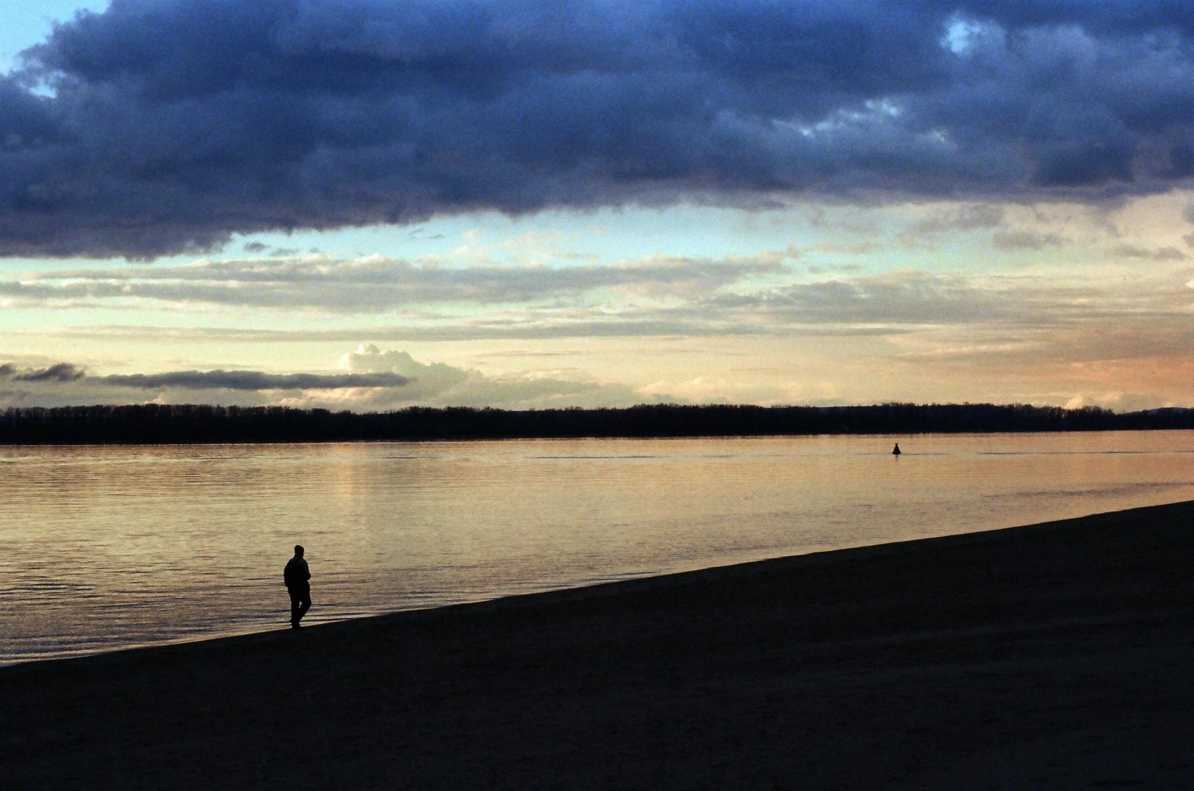 a person standing on a beach next to a body of water, wide river and lake, at dusk, people walking in the distance, landscape photo