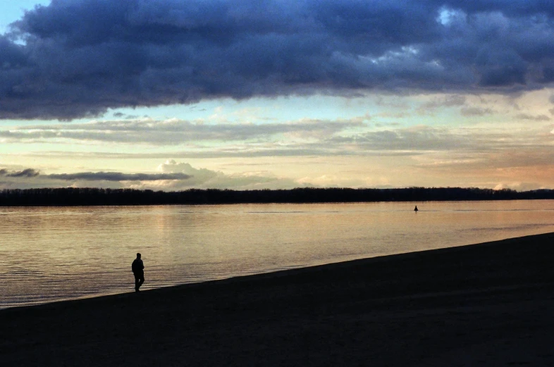 a person standing on a beach next to a body of water, wide river and lake, at dusk, people walking in the distance, landscape photo