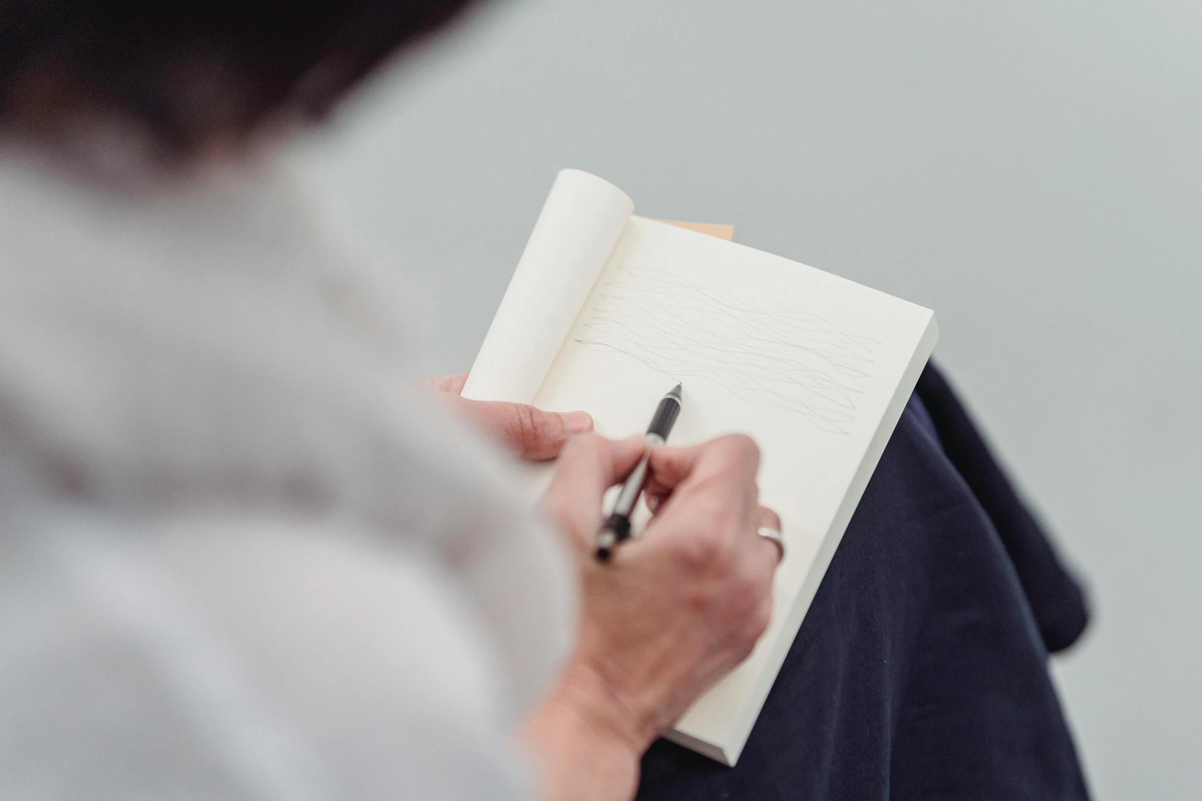 a woman holding a pen and writing in a notebook, inspired by Agnes Martin, sitting down casually, middle shot, pen draw, lightweight