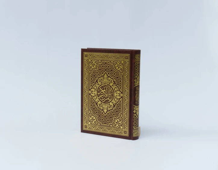 a book sitting on top of a white surface, hurufiyya, gold filigree, medium wide front shot, dall-e 2, front