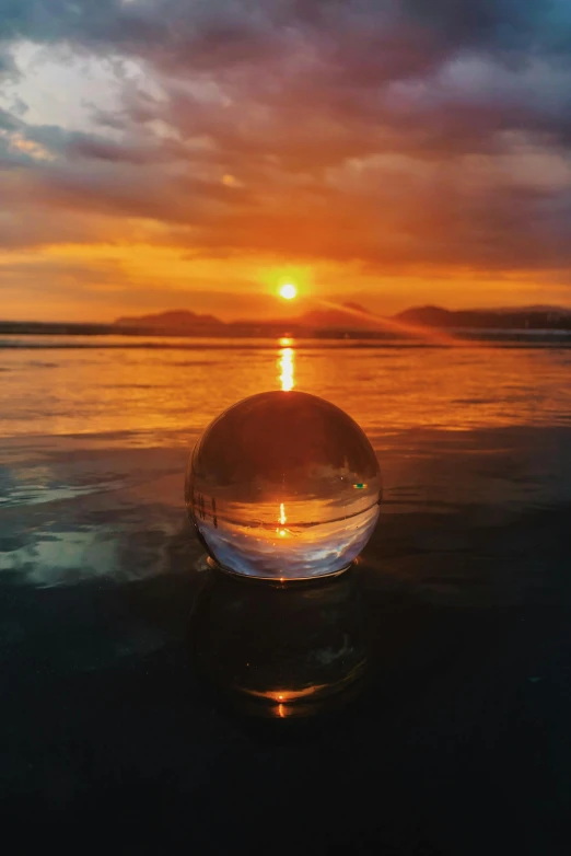 a glass ball sitting on top of a beach, during a sunset, 8k award-winning photograph, sun puddle, golden bay new zealand