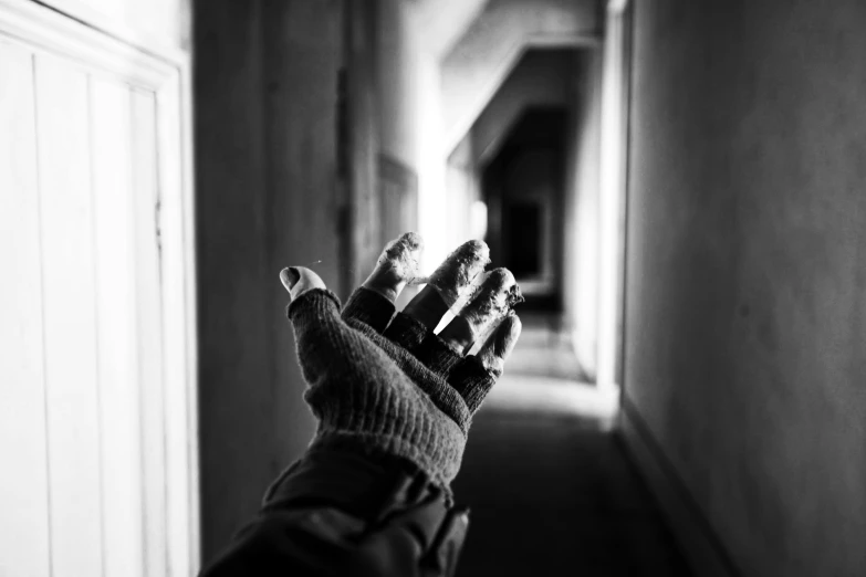 a black and white photo of a person's hand in a hallway, derelict, wearing gloves, natural light outside, tourist photo