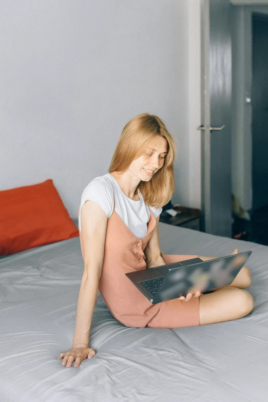 a woman sitting on a bed using a laptop computer, trending on reddit, wearing a light shirt, a redheaded young woman, smooth feature, modern photo