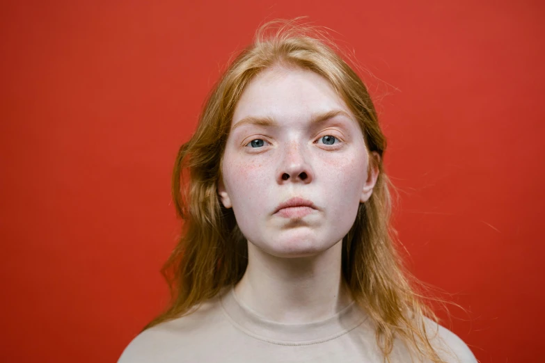 a close up of a woman with freckles on her face, a character portrait, trending on pexels, in red background, teenage girl, pale bluish skin, flowing ginger hair