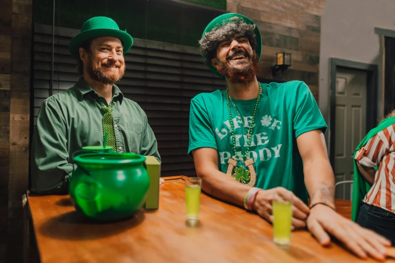 a couple of men sitting next to each other at a table, by Meredith Dillman, pexels contest winner, symbolism, wearing green tophat, 🍸🍋, clover, laughing out loud