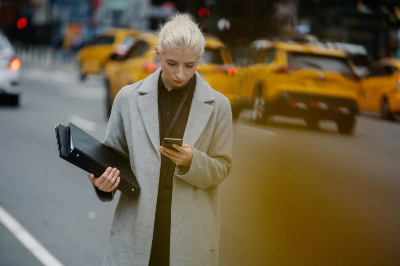 a woman walking down the street looking at her cell phone, pexels, yellow and charcoal leather, holding a clipboard, a blond, thumbnail