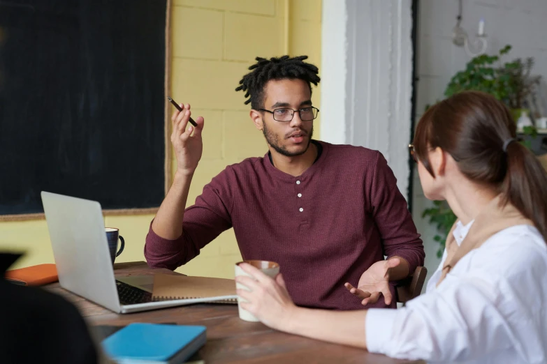 a man and a woman sitting at a table in front of a laptop, varying ethnicities, teaching, profile image, high quality image