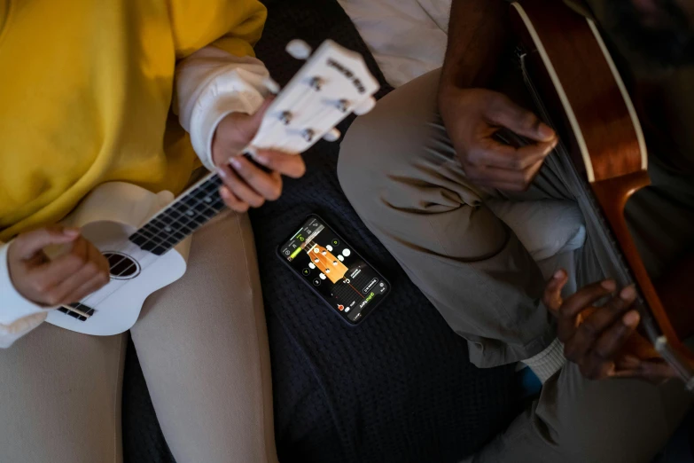 a close up of a person holding a guitar, phone in hand, two buddies sitting in a room, mobile app, top angle