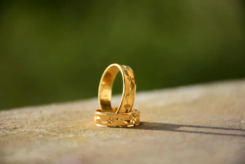 a couple of wedding rings sitting on top of a wooden table, unsplash, gold madhubani, in the sun, shot on sony a 7, hyperrealistic image