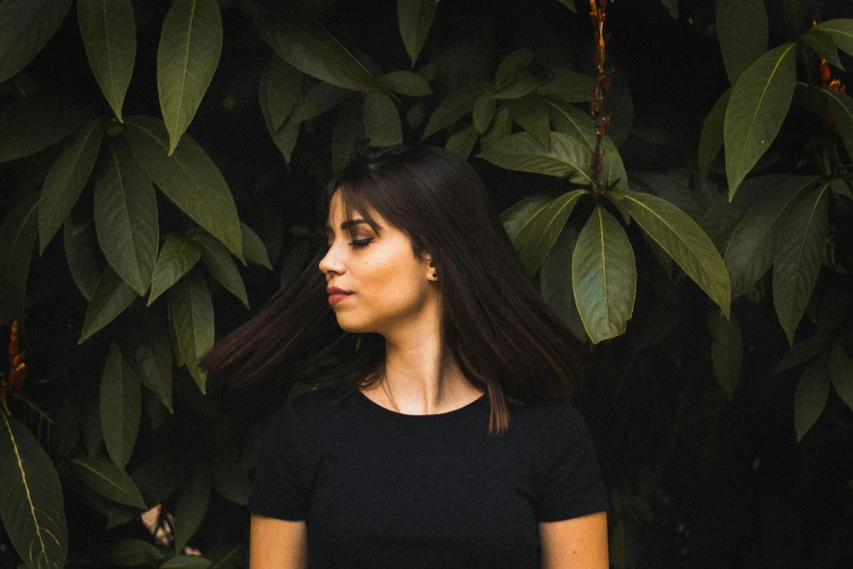 a woman standing in front of a bunch of leaves, an album cover, inspired by Elsa Bleda, pexels contest winner, realism, wearing a black t-shirt, perfect silky straight hair, headshot profile picture, elegant profile pose