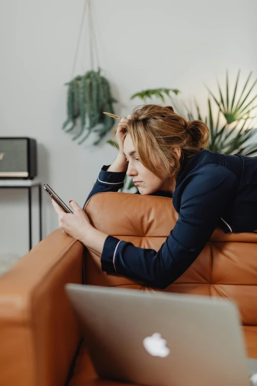 a woman laying on a couch using a laptop, trending on pexels, looking at his phone, disappointed, leather couch, in a navy blue sweater