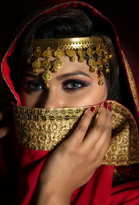a woman with a red veil covering her face, an album cover, inspired by Osman Hamdi Bey, pexels contest winner, big gold eyes, tribal clothing, gold encrustations, arab inspired