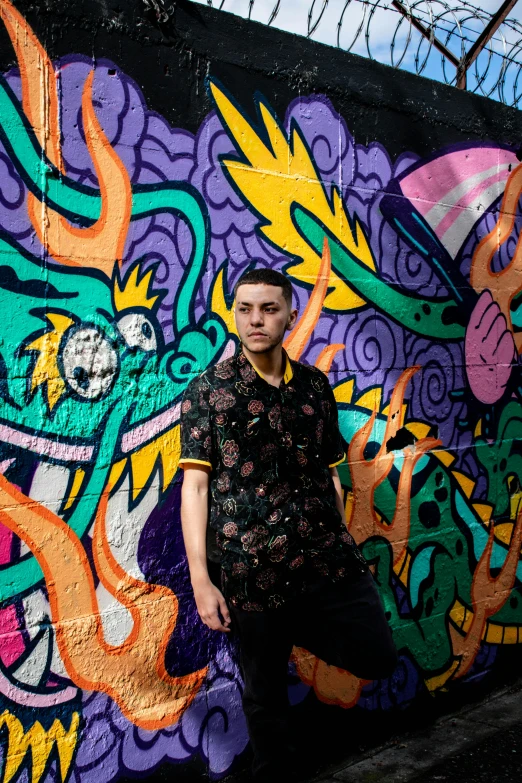 a man standing in front of a colorful wall, an album cover, inspired by Eddie Mendoza, graffiti, looking towards camera, patterned clothing, (night), young adult male