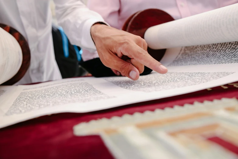 a man holding a roll of paper on top of a table, a silk screen, by Elias Goldberg, unsplash, holy ceremony, sholim, multiple stories