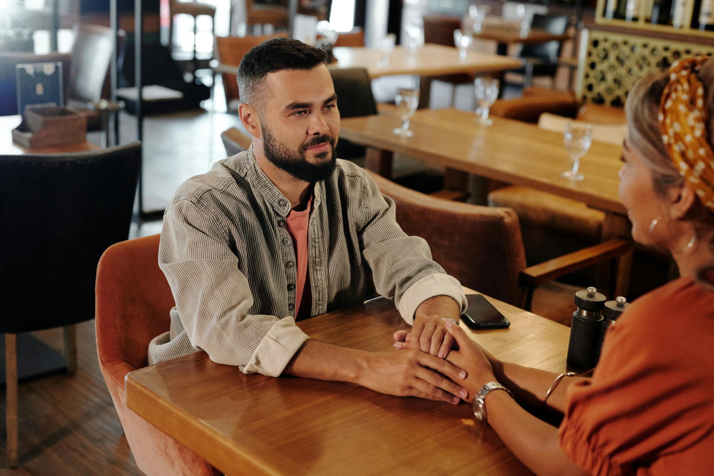 a man and a woman sitting at a table, trending on pexels, hurufiyya, holding hand, brown, casually dressed, talking