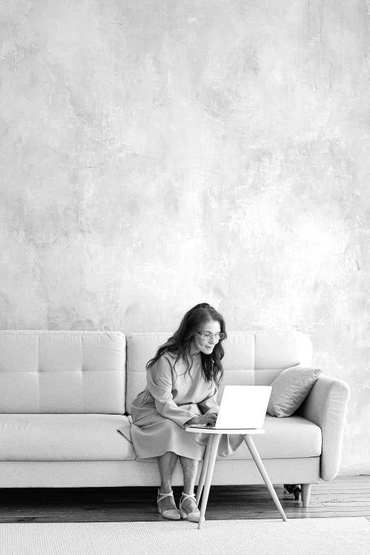 a woman sitting on a couch using a laptop, a black and white photo, by Lucia Peka, pexels contest winner, minimalism, monochromatic background, 15081959 21121991 01012000 4k, romance, white furniture