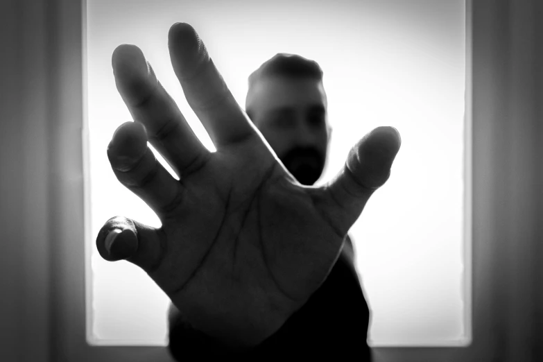 a person holding their hand up in front of a window, a black and white photo, by Jan Rustem, pexels, visual art, 30 year old man, threatening pose, five fingers, studio shoot