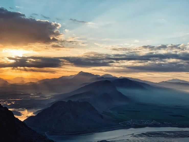 a person standing on top of a mountain next to a body of water, by Sebastian Spreng, pexels contest winner, romanticism, sunset panorama, “ aerial view of a mountain, hazy sunset with dramatic clouds, multiple stories