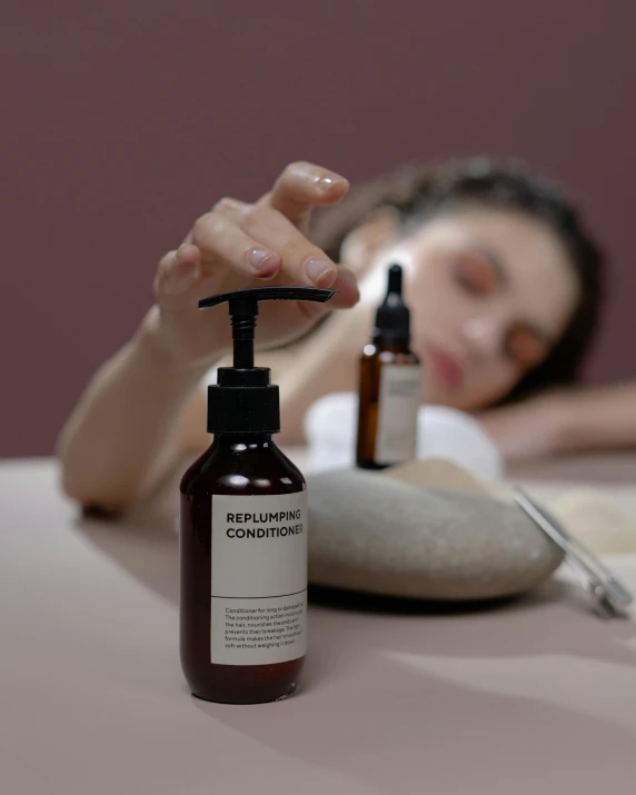 a woman laying on a bed next to a bottle of hand sanitizer, by Julia Pishtar, touching heads, set on singaporean aesthetic, with textured hair and skin, left hand propping up the head