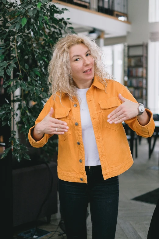 a woman in a yellow jacket talking to another woman, by Zofia Stryjenska, pexels, curly blonde hair | d & d, stands in center with open arms, cropped shirt with jacket, russian academic