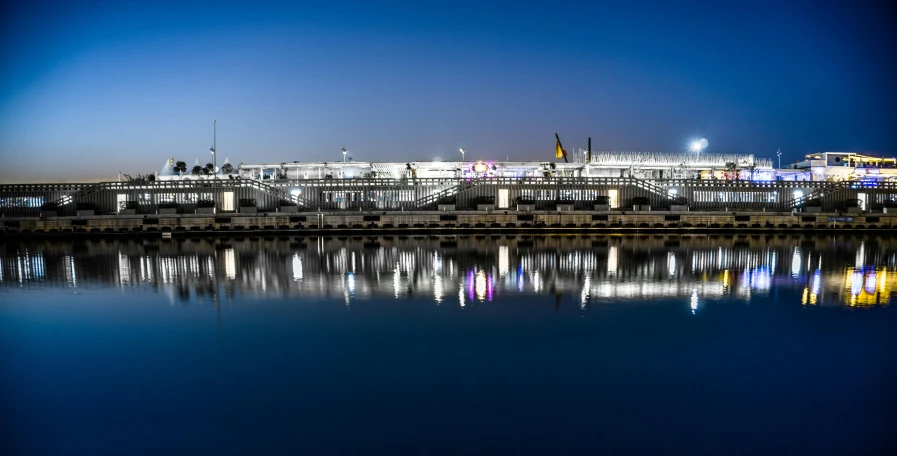 a bridge over a body of water at night, a tilt shift photo, pexels contest winner, bauhaus, stadium setting, terminal, twilight ; wide shot, neon reflections