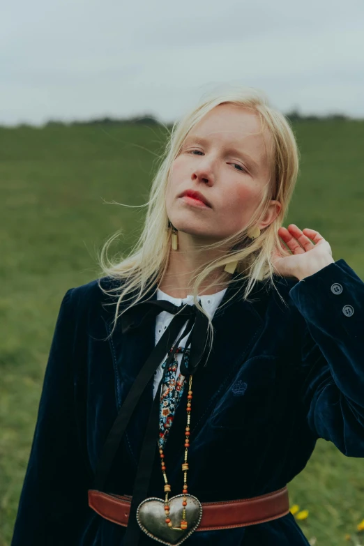 a woman standing on top of a lush green field, an album cover, by Anna Boch, unsplash, renaissance, pale hair, wearing a blue jacket, jewel, greta thunberg