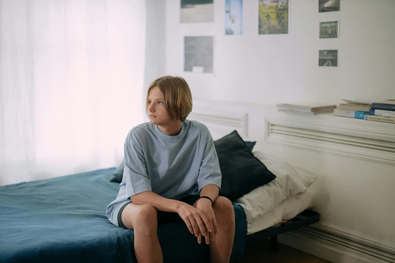 a woman sitting on a bed in a bedroom, trending on unsplash, hyperrealism, portrait of 14 years old boy, blue shirt, sad lonely mellow vibes, with short hair